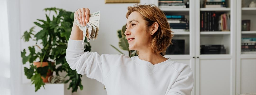 lady holding money in hands while working from home on laptop